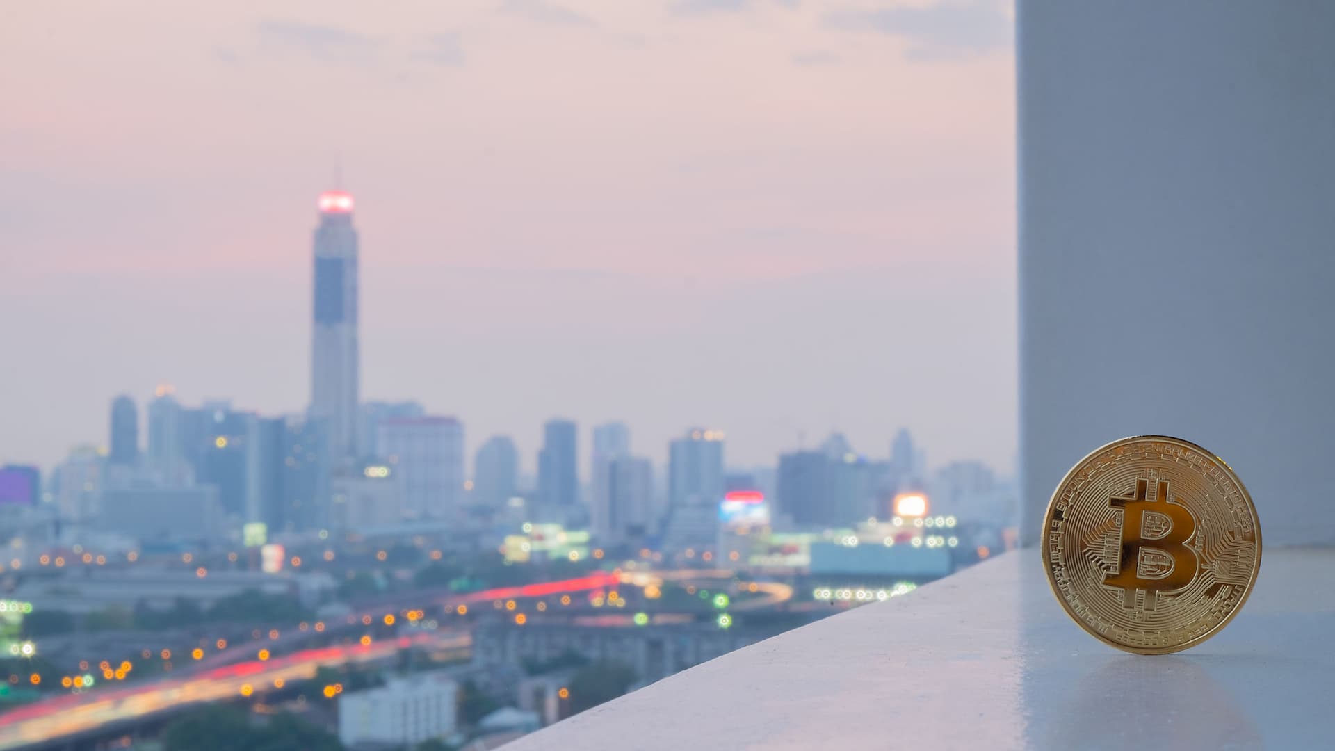 Image of a golden bitcoin standing on a floor with blurred cityscape in the background