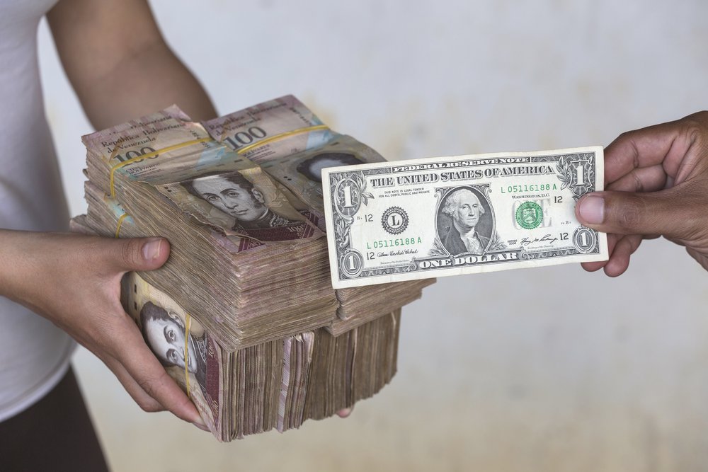 Hands exchange one US dollar for thousands of Bolivars.