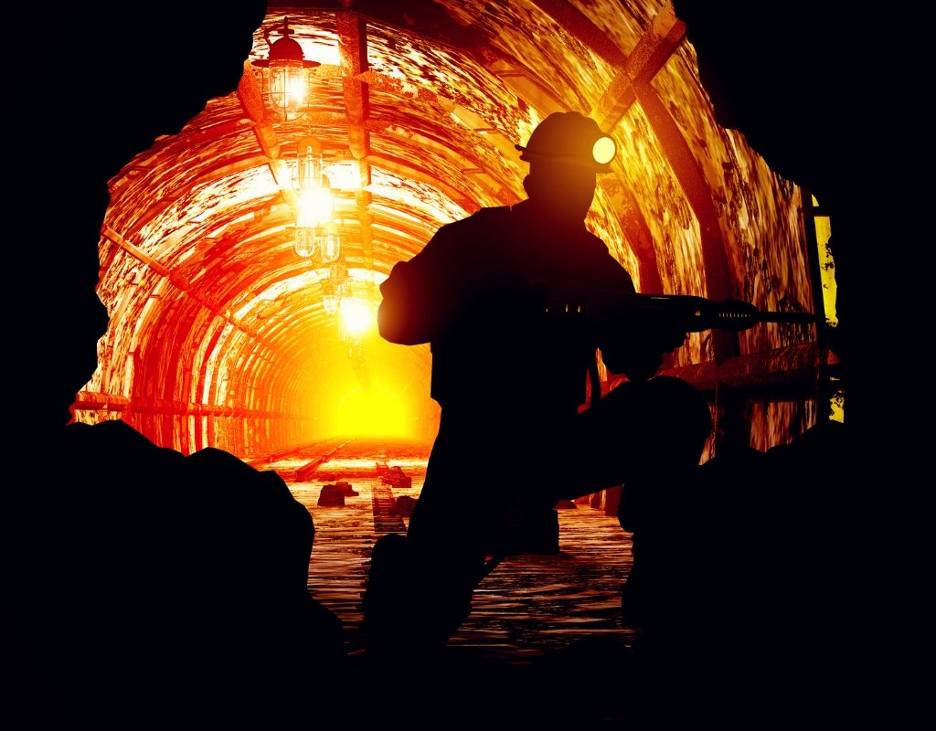 A backlit miner drills into rock.