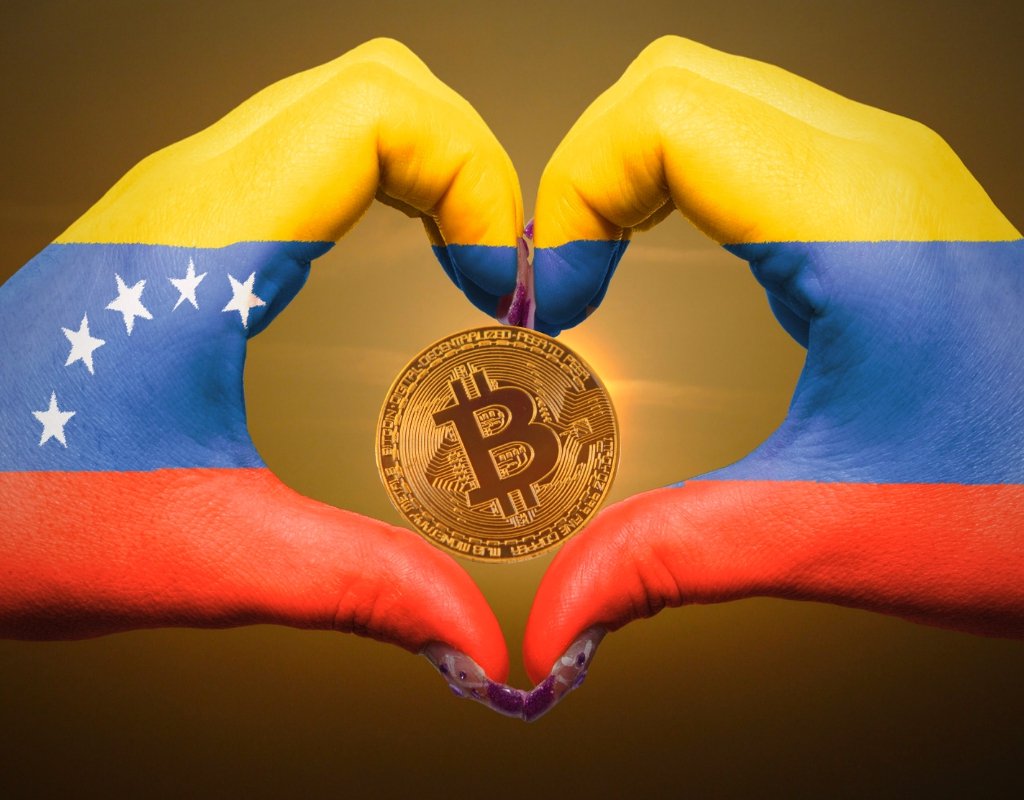 Hands make a shape of a heart around a bitcoin, painted with the colours of Venezuela's national flag.